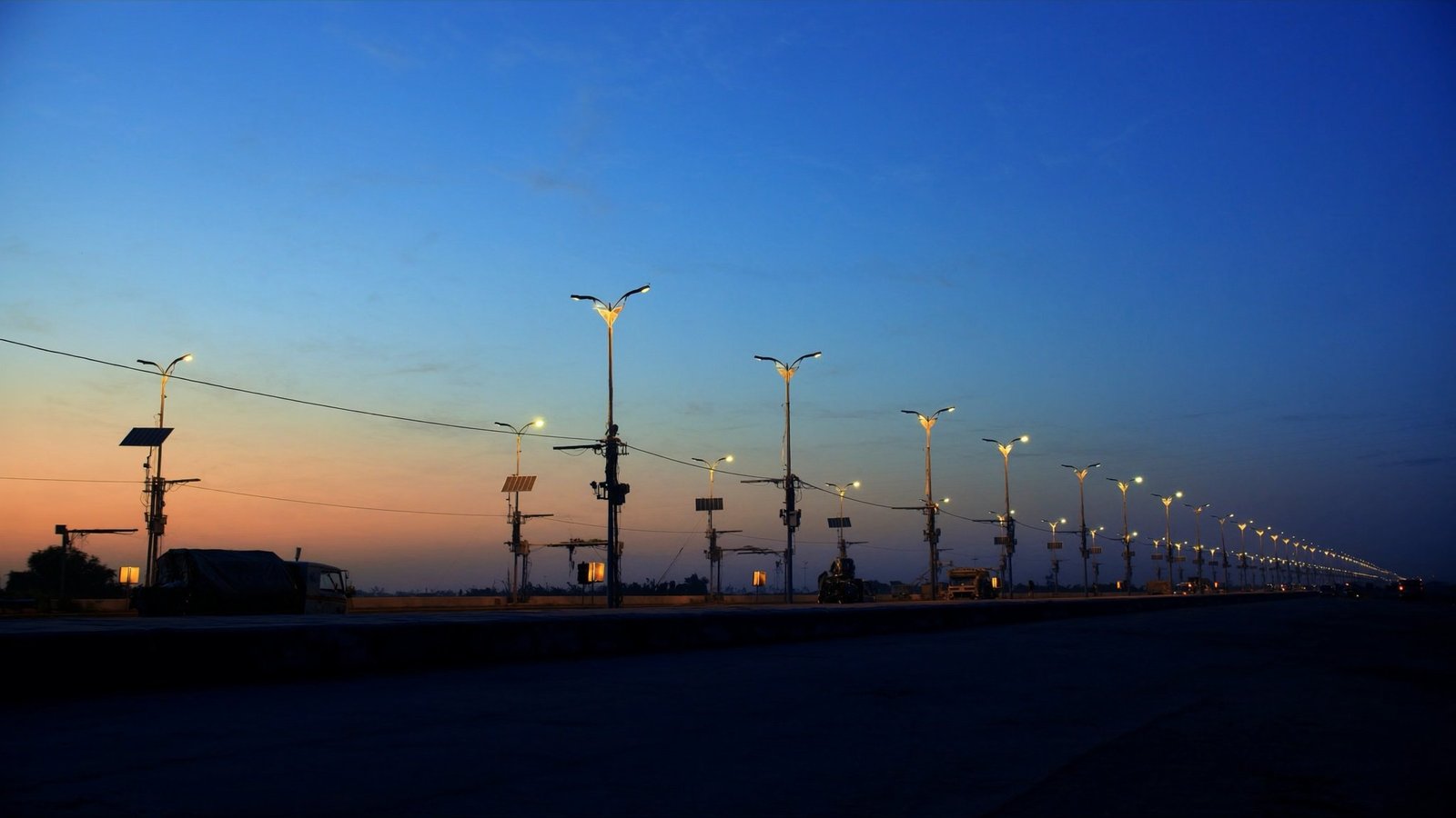 Row of street lights along an Indian highway at dusk, some with solar panels